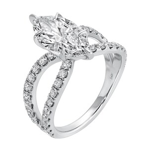 May include: A white gold ring featuring a large, marquise-cut diamond as the centerpiece. The band splits into two, each lined with smaller diamonds, creating a sparkling, elegant design. The ring is set against a white background.