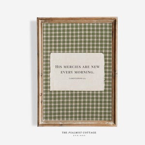 May include: A framed print with a green and white plaid pattern. The print displays the text "HIS MERCIES ARE NEW EVERY MORNING. LAMENTATIONS 3:23" on a textured, off-white paper. The frame is light brown.