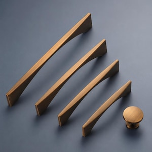 May include: A set of bronze-toned cabinet handles and a knob, displayed on a blue background. The set includes four pull handles of varying lengths and a circular knob. The handles have a contemporary, geometric design.