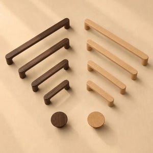 Puede incluir: Una colección de herrajes de madera para muebles que incluye cuatro tiradores rectangulares de diferentes longitudes y un pomo circular en acabados de madera marrón oscuro y bronceado claro, dispuestos en dos columnas sobre un fondo neutro.