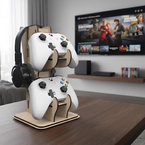 Może przedstawiać: Drewniany stojak na kontrolery do gier i zestaw słuchawkowy. Stojak mieści dwa białe kontrolery i czarny zestaw słuchawkowy. Stojak wykonany jest z jasnego drewna i stoi na ciemnobrązowym stole. W tle znajduje się telewizor.