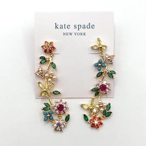Puede incluir: Un par de pendientes Kate Spade con un diseño floral. Los pendientes tienen una base de metal dorado con piedras preciosas de colores y perlas de imitación. Los pendientes tienen forma de vid floral con flores en tonos rojos, rosas, naranjas, azules y morados.