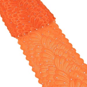 May include: Bright orange lace fabric with a floral pattern and scattered rhinestones. The lace is folded over, showing the intricate design and texture. This fabric is suitable for various craft and sewing projects.