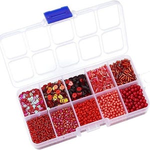 May include: A clear plastic organizer with a blue clasp, filled with various red and pink beads, sequins, and bugle beads. The compartments hold different shapes and sizes, perfect for crafting and jewelry making.