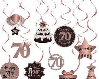 May include: A collection of rose gold and black 70th birthday decorations, including balloons, a cake, star-shaped ornaments, and a gift box. The decorations are suspended with pink ribbons, creating a festive atmosphere. The words "Happy 70th Birthday" and "Seventy" are visible.