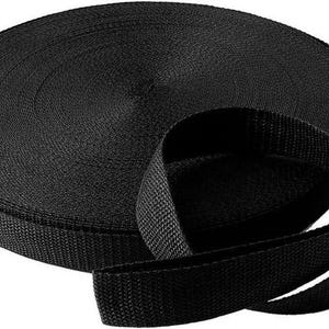 May include: A roll of black nylon webbing. The webbing is tightly woven and appears durable. The roll is circular, with a portion unrolled, showing the flat, sturdy strap. Ideal for various crafting and utility projects.