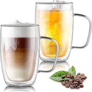 May include: Two clear glass mugs with handles, one filled with a layered coffee drink and the other with a golden beverage and ice cubes. Coffee beans and a green leaf are in the foreground. The mugs are double-walled.