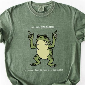 A green t-shirt with a cartoon frog and text printed on it.
