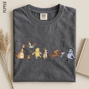 A gray t-shirt with a line of colorful cartoon animal characters printed on it, including a kangaroo, eagle, bear, lion, pig, and elephant.