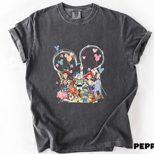 A gray t-shirt with a colorful graphic design featuring characters from the Toy Story movie, including Woody, Buzz Lightyear, and other beloved characters.