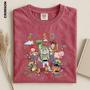 A red t-shirt with a colorful graphic design featuring characters from the Toy Story movie, including Woody, Buzz Lightyear, and other beloved characters.