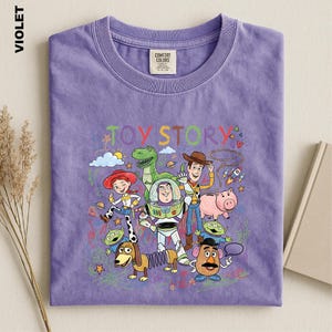 A purple t-shirt with a colorful illustration of characters from the Toy Story movie, including Woody, Buzz Lightyear, and other beloved characters.