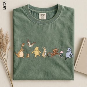 A green t-shirt with a line of cartoon animal characters printed on it, including a kangaroo, eagle, bear, lion, and other animals.