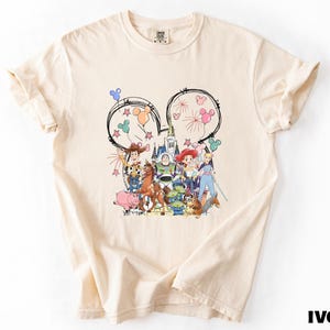 A white t-shirt with a colorful graphic design featuring various cartoon characters and Disney-themed elements.