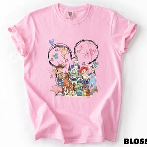 A pink t-shirt with a colorful graphic design featuring various cartoon characters and Disney-themed elements.