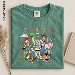 A green t-shirt with a colorful graphic design featuring characters from the Toy Story movie, including Woody, Buzz Lightyear, and other beloved characters.