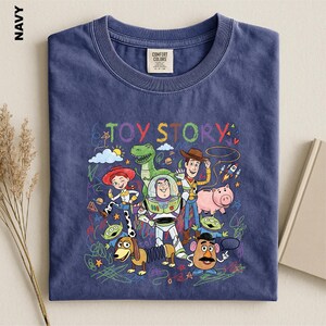 A navy blue t-shirt with a colorful graphic design featuring characters from the Toy Story movie, including Woody, Buzz Lightyear, and other beloved characters.