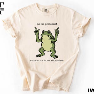 a white t-shirt with a graphic design of a frog making a hand gesture and the text "me. no problem!" printed on it.