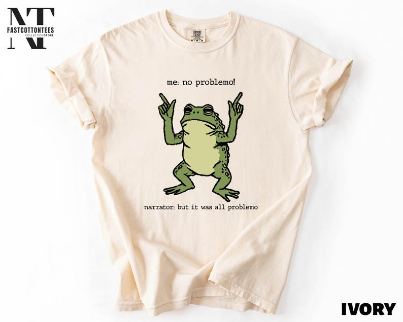 a white t-shirt with a graphic design of a frog making a hand gesture and the text "me. no problem!" printed on it.