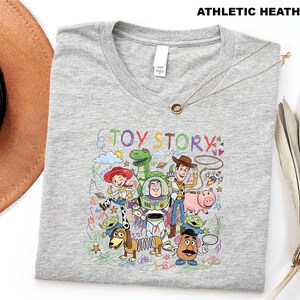 A gray t-shirt with a colorful graphic design featuring characters from the Toy Story movie, including Woody, Buzz Lightyear, and other beloved characters.