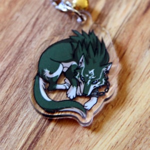 Puede incluir: Un llavero de lobo verde con una cadena plateada y un abalorio dorado. El lobo está enroscado y tiene la panza blanca.