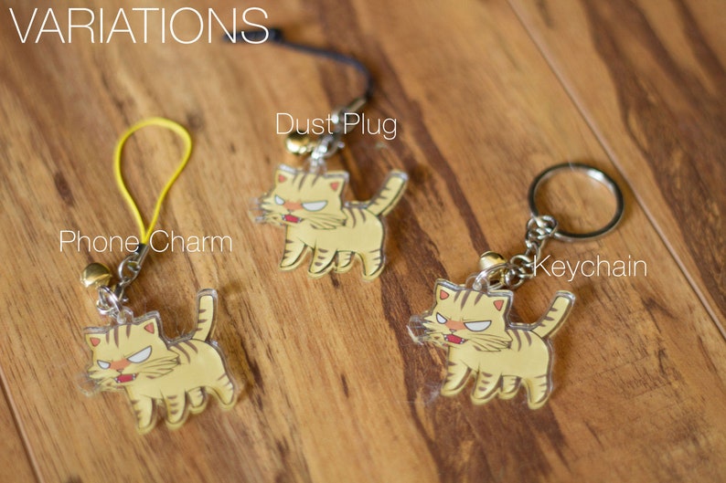 May include: Three variations of a keychain featuring a cartoon cat with a yellow and orange striped pattern. The keychain is available as a phone charm, dust plug, and keychain.