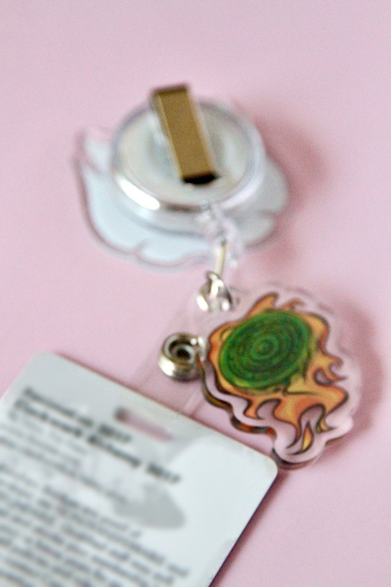 May include: A clear plastic badge holder with a retractable reel and a gold clip. The holder has a green and orange cartoon design of a swirling vortex.