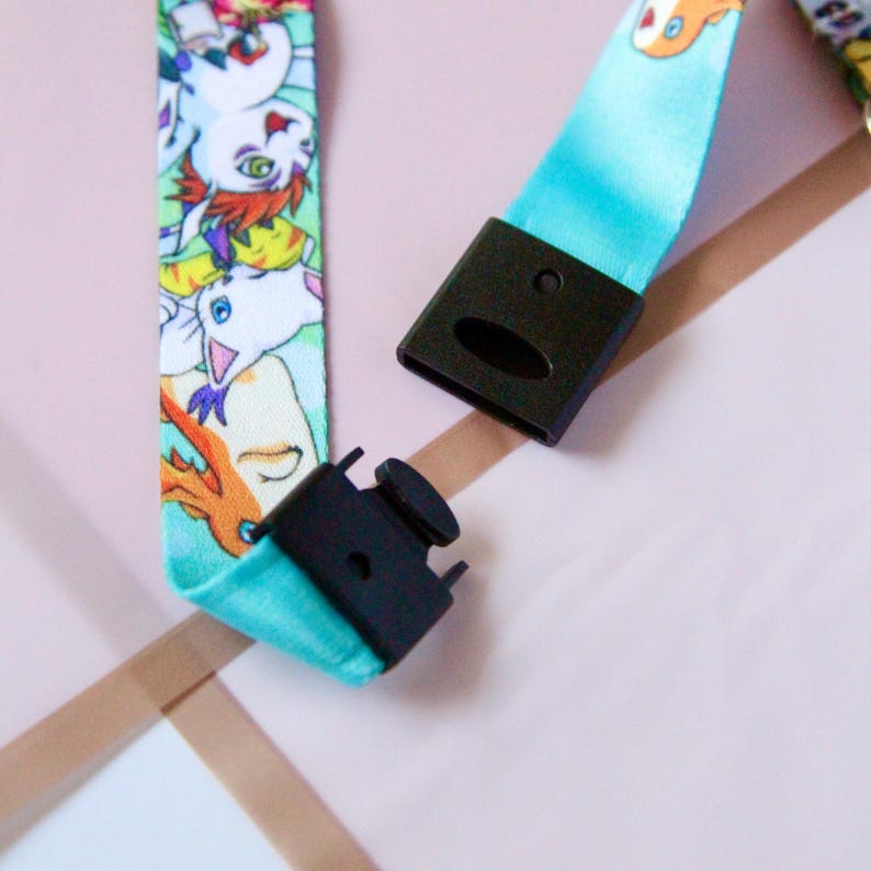 May include: A turquoise blue lanyard with a colorful cartoon print of various characters. The lanyard has a black plastic clip on each end.