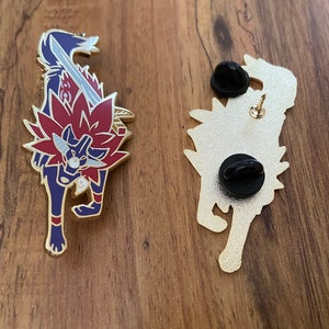 May include: Gold-colored enamel pin featuring a red and blue wolf with a sword. The back of the pin shows the wolf's silhouette with a pin back.