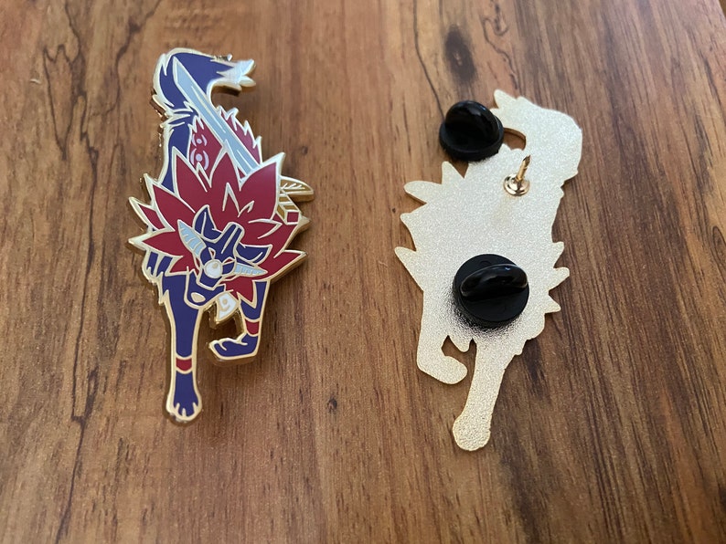 May include: Gold-colored enamel pin featuring a red and blue wolf with a sword. The back of the pin shows the wolf's silhouette with a pin back.