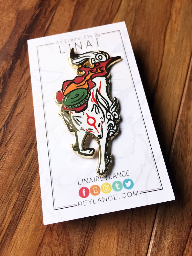 May include: An enamel pin by LINAI featuring a white fox with red and orange flames, a green and gold disc on its back, and a red circle with a white symbol on its chest. The pin is on a white card with the text "An Enamel Pin By LINAI" and "LINAIREYLANCE" with social media icons and a website address.