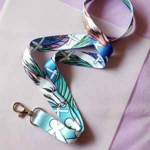 May include: A blue and white lanyard with a white fox design and green leaves. The lanyard has a silver metal clip.
