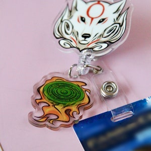 May include: A white wolf with a red circle on its forehead and a green and yellow swirl design on a retractable badge holder.