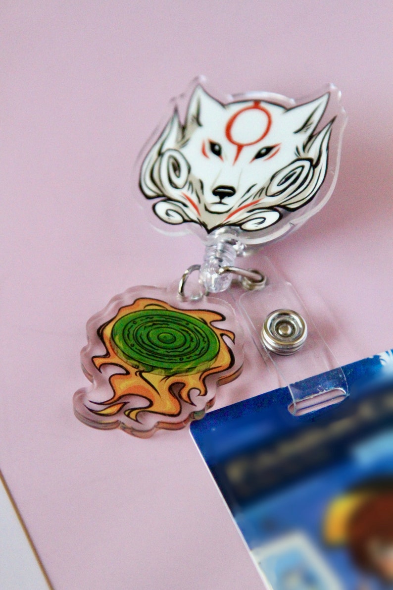 May include: A white wolf with a red circle on its forehead and a green and yellow swirl design on a retractable badge holder.