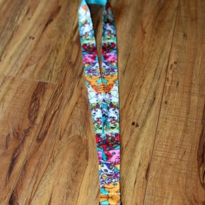 May include: A turquoise lanyard with a colorful print of cartoon characters. The lanyard has a silver metal clip.