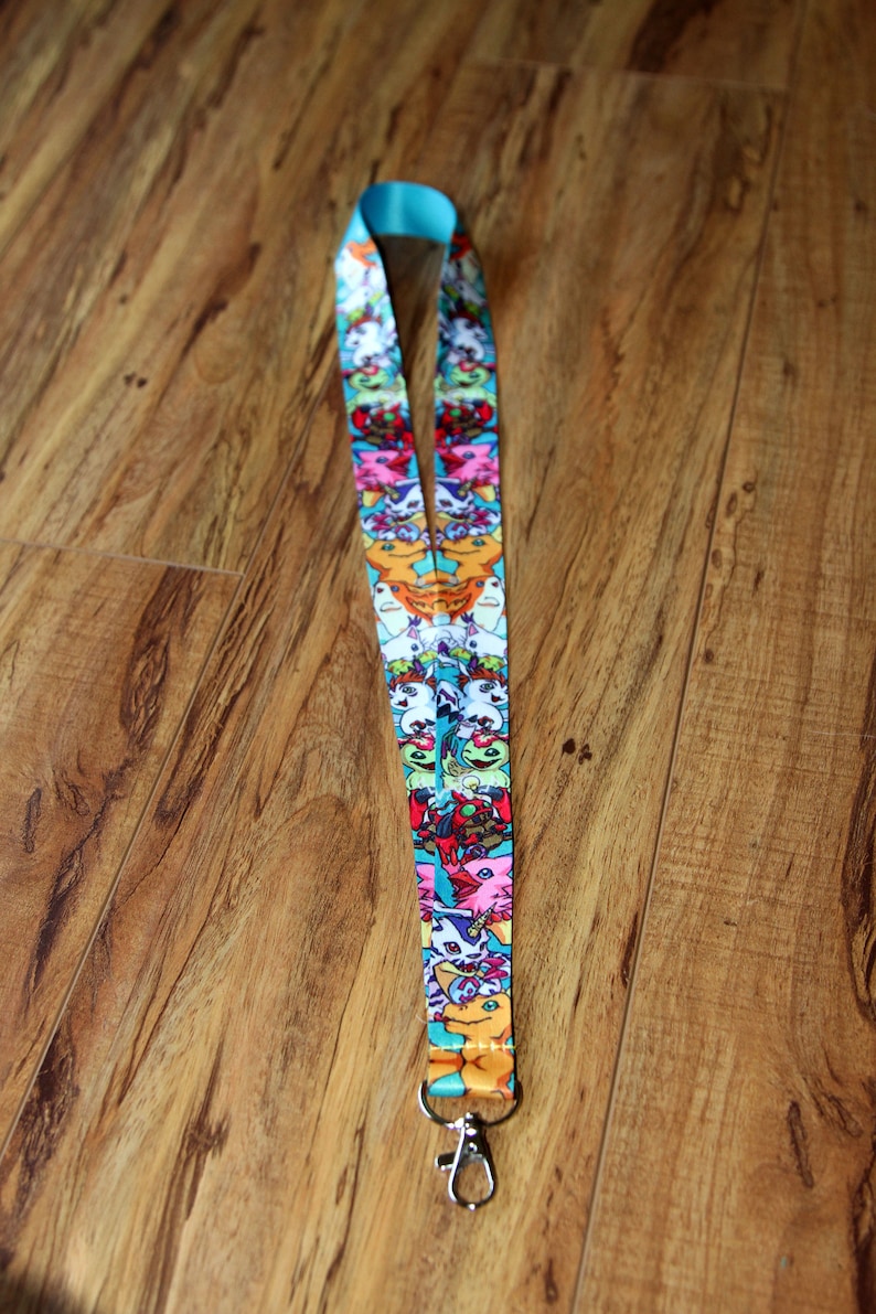 May include: A turquoise lanyard with a colorful print of cartoon characters. The lanyard has a silver metal clip.