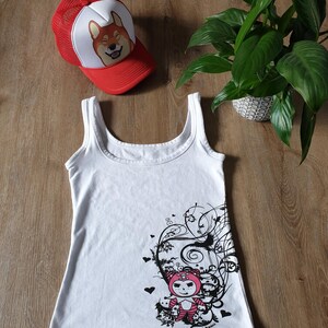 May include: White tank top with a black and white graphic print of a cartoon character with pink hair and a black and white swirl design. The character is wearing a red and white outfit. The tank top has a black and white text label that says "Black Manga".