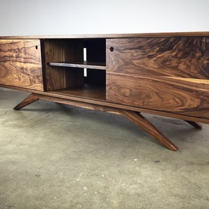 Puede incluir: Un centro de entretenimiento de estilo moderno de mediados de siglo hecho de madera de nogal con puertas corredizas y estantes abiertos. El gabinete tiene un color marr&oacute;n intenso y presenta patas anguladas.