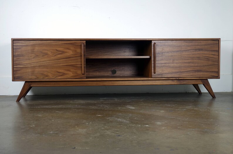 May include: A mid-century modern walnut wood entertainment center with two doors and a shelf. The doors have a wood grain pattern and the legs are angled.