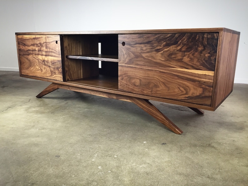 Puede incluir: Un centro de entretenimiento de estilo moderno de mediados de siglo hecho de madera de nogal con puertas corredizas y estantes abiertos. El gabinete tiene un color marr&oacute;n intenso y presenta patas anguladas.