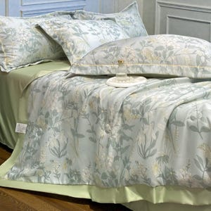May include: A bed with a light green fitted sheet and a floral patterned comforter and pillowcases. The comforter and pillowcases have a light blue background with white and yellow floral designs. A decorative bottle sits on a white tray.