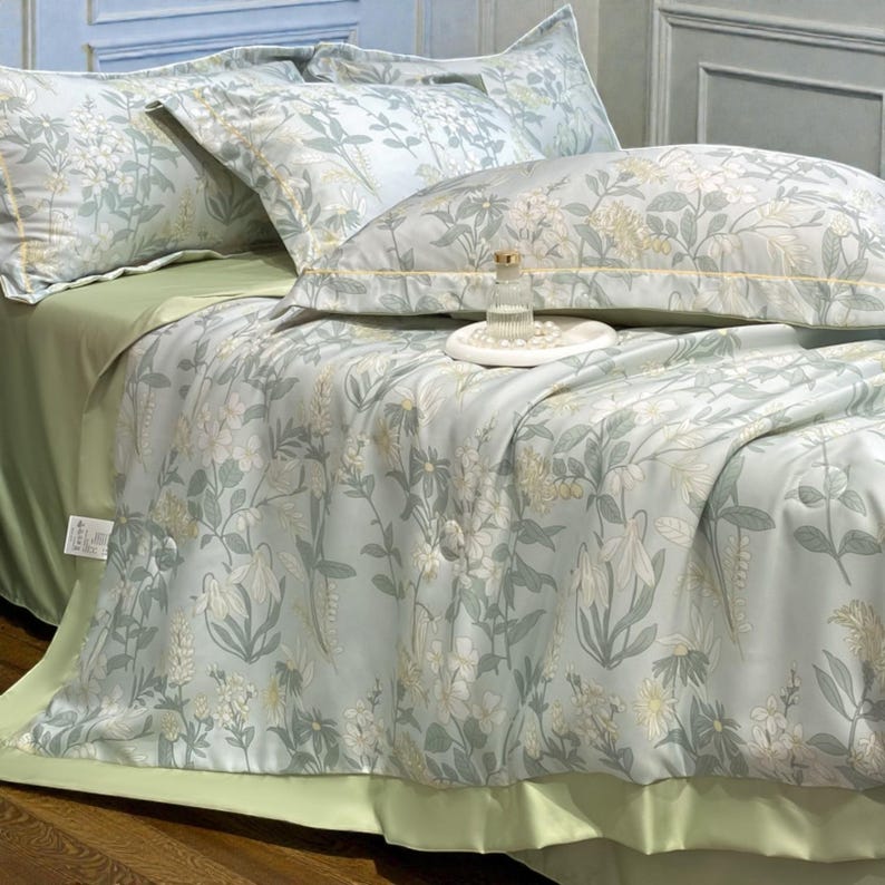 May include: A bed with a light green fitted sheet and a floral patterned comforter and pillowcases. The comforter and pillowcases have a light blue background with white and yellow floral designs. A decorative bottle sits on a white tray.