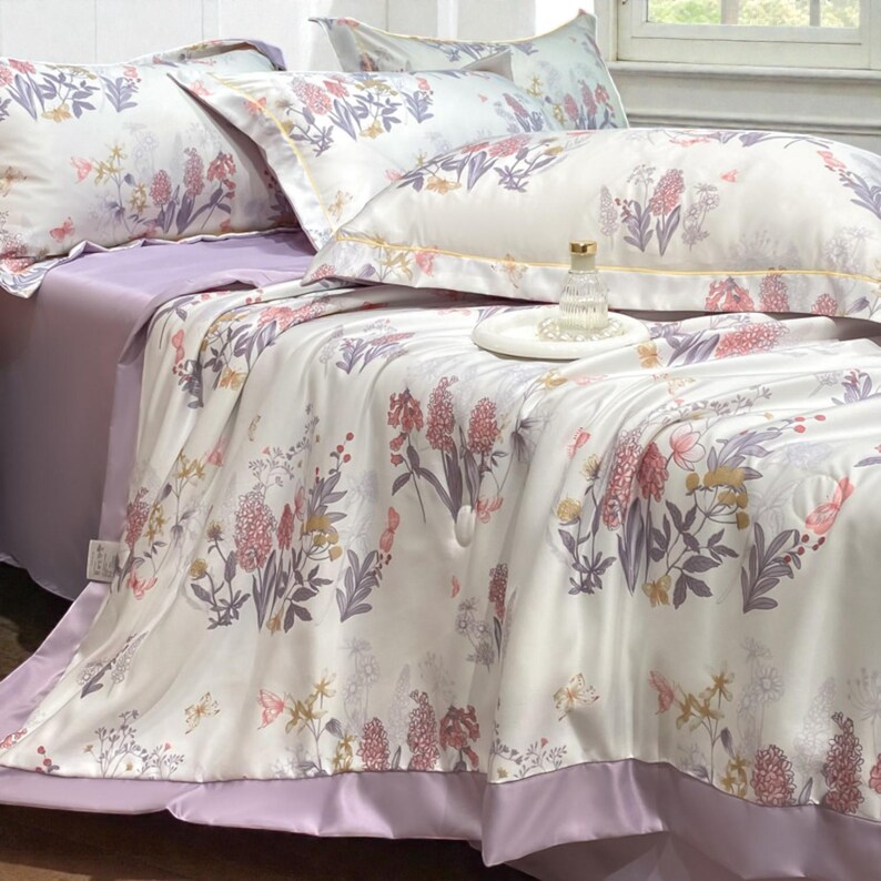 May include: A bed set featuring a floral pattern in shades of pink, purple, and yellow on a white background. The set includes a comforter, pillowcases, and a solid purple sheet. The bedding has a satin finish.