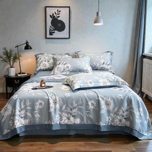 May include: A light blue floral bed set featuring large white flowers and gray leaves. The set includes a comforter, pillows, and a bed skirt. The bedding is arranged on a bed in a bedroom setting.