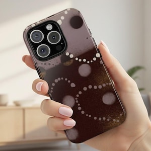 May include: A smartphone case with a brown and purple abstract design. The case features a pattern of white dots and circles. The phone case is held in a hand.