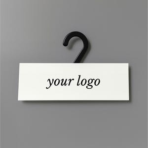 May include: A black plastic clothing hanger with a white rectangular sign. The sign displays the text "your logo" in a simple, elegant font. The background is a solid gray.