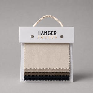 Puede incluir: Un conjunto de muestras de tela con cuatro piezas textiles rectangulares apiladas en tonos crema, beige, marrón y negro. La tarjeta de encabezado blanca muestra el texto HANGER SWATCH en negro y dorado, asegurado con dos tornillos metálicos.