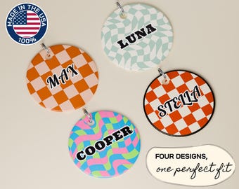 May include: Four colorful pet tag designs with names: Max, Luna, Stella, and Cooper. Each tag is round with a unique checkered or wavy pattern in orange, pink, blue, and green. The tags have a silver ring for attachment. The text "Made in the USA" is also visible.
