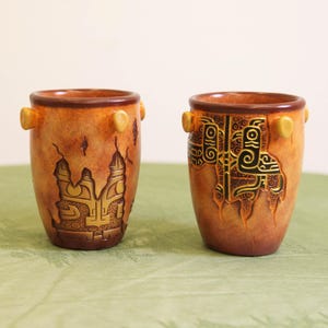 May include: Two ceramic vases with a textured, aged appearance. The vases are primarily brown with darker brown rims and handles. One vase features a gold-colored castle design, while the other displays a black and gold geometric pattern. Each vase is approximately 4 inches tall.