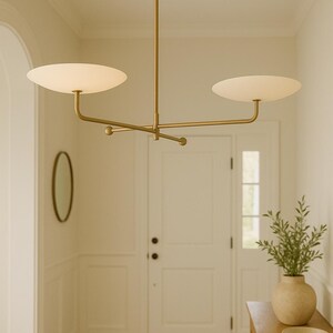 Modern brass linear chandelier with two dish-shaped shades hanging above a minimalist gray and white bedroom interior
Handmade brass pendant light fixture with dual disc shades in a modern bedroom with neutral décor
Luxury brushed brass two-arm linear chandelier installed above a bed in a contemporary minimalist room
Mid century modern brass ceiling light with two flat dome shades illuminating a cozy bedroom interior